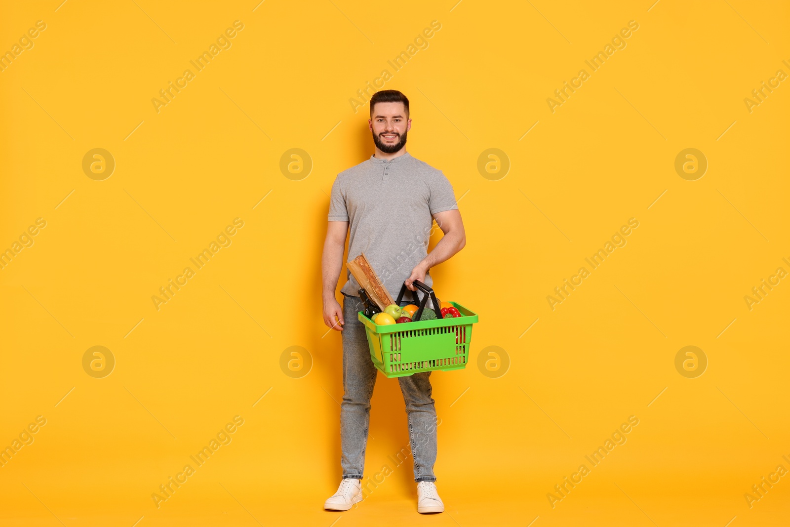 Man with shopping basket full of products on orange background Photo of Man with shopping basket full of products on orange background