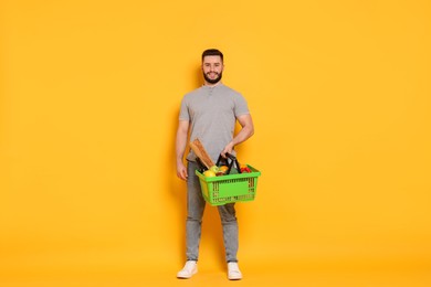 Photo of Man with shopping basket full of products on orange background