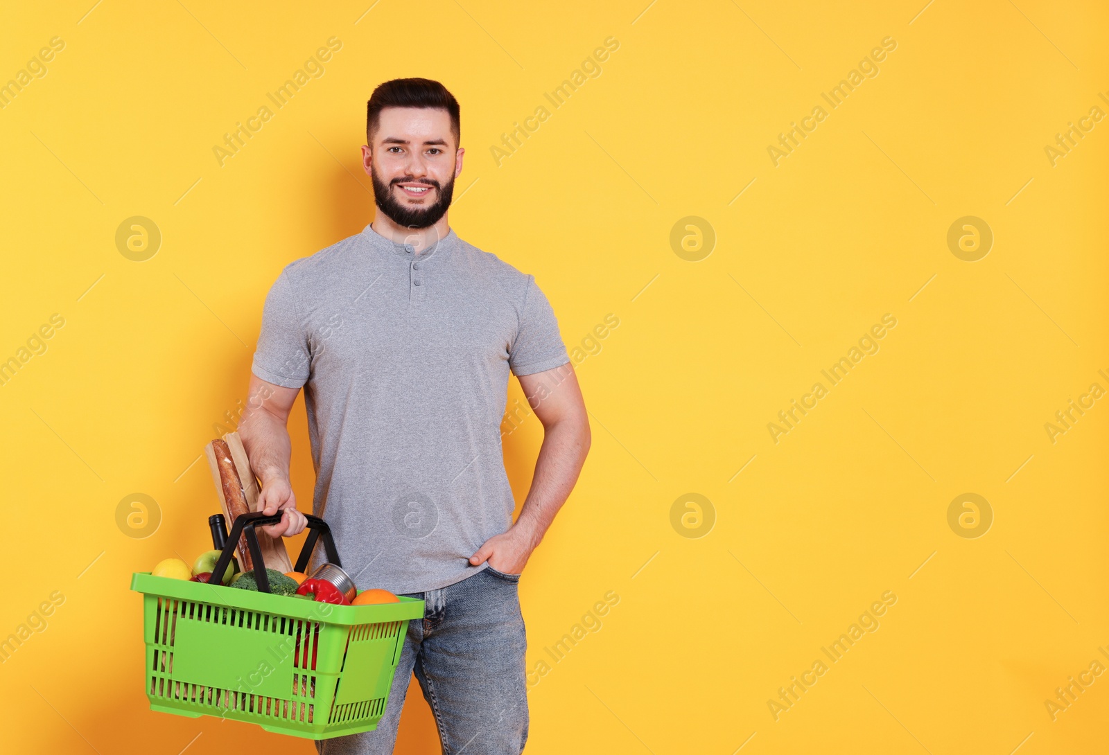 Man with shopping basket full of products on orange background, space for text Photo of Man with shopping basket full of products on orange background, space for text