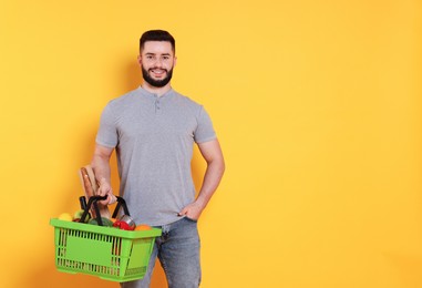 Photo of Man with shopping basket full of products on orange background, space for text