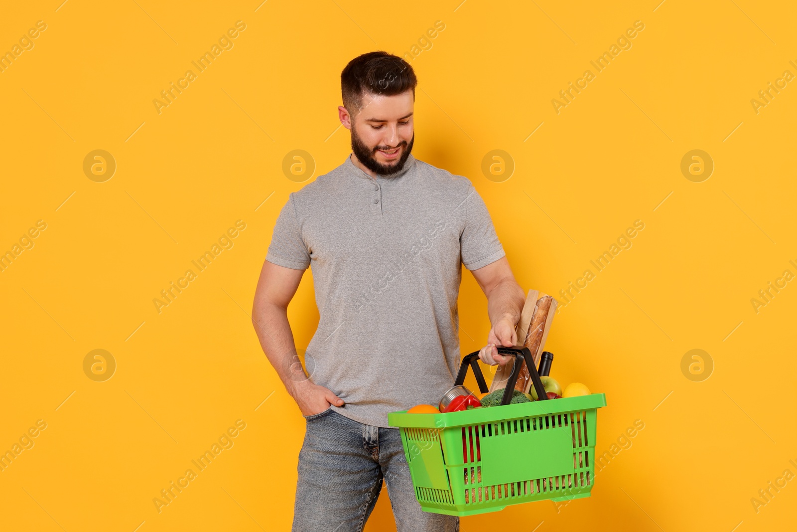 Man with shopping basket full of products on orange background Photo of Man with shopping basket full of products on orange background