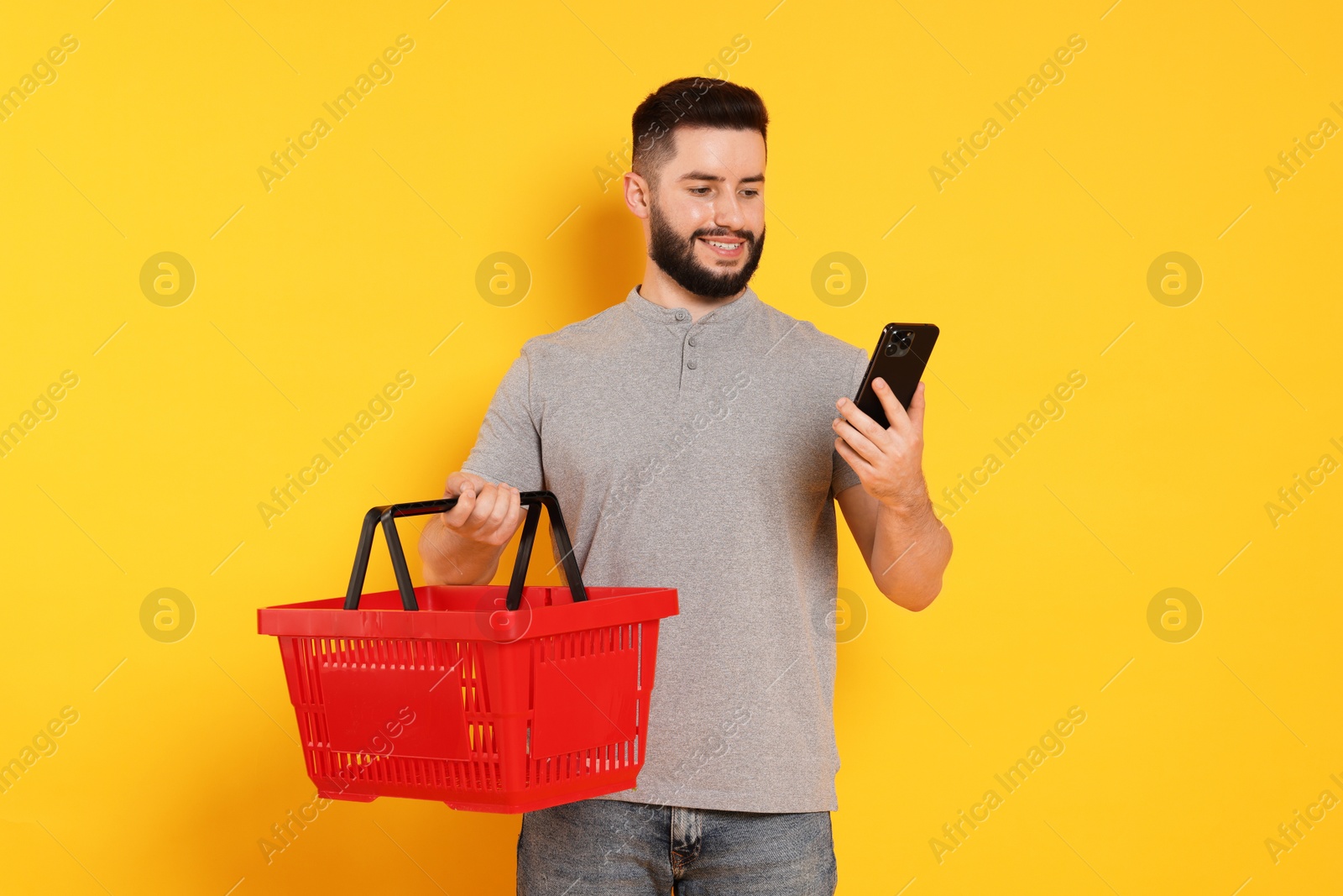 Man with empty shopping basket and smartphone on orange background Photo of Man with empty shopping basket and smartphone on orange background