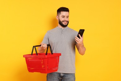 Photo of Man with empty shopping basket and smartphone on orange background