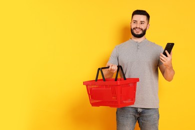 Photo of Man with empty shopping basket and smartphone on orange background, space for text