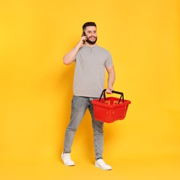 Photo of Man with empty shopping basket talking on smartphone against orange background
