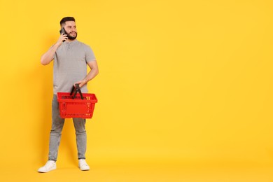Photo of Man with empty shopping basket talking on smartphone against orange background, space for text