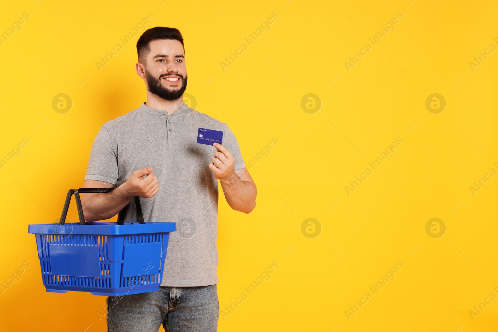 Man with empty shopping basket and credit card on orange background, space for text Photo of Man with empty shopping basket and credit card on orange background, space for text