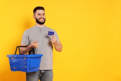 Photo of Man with empty shopping basket and credit card on orange background, space for text