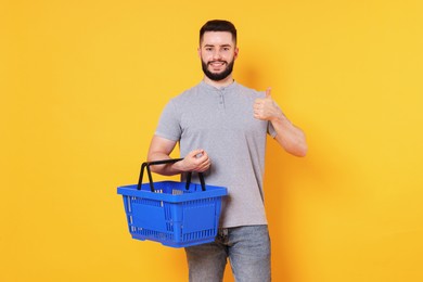 Photo of Man with empty shopping basket showing thumbs up on orange background