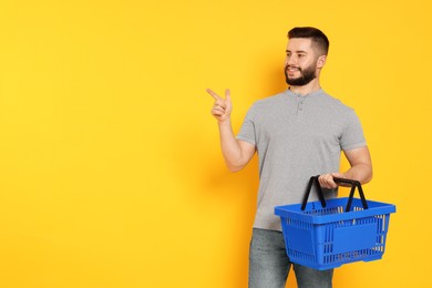 Photo of Man with empty shopping basket pointing at something on orange background, space for text