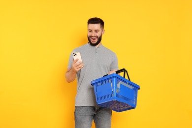 Photo of Man with empty shopping basket and smartphone on orange background