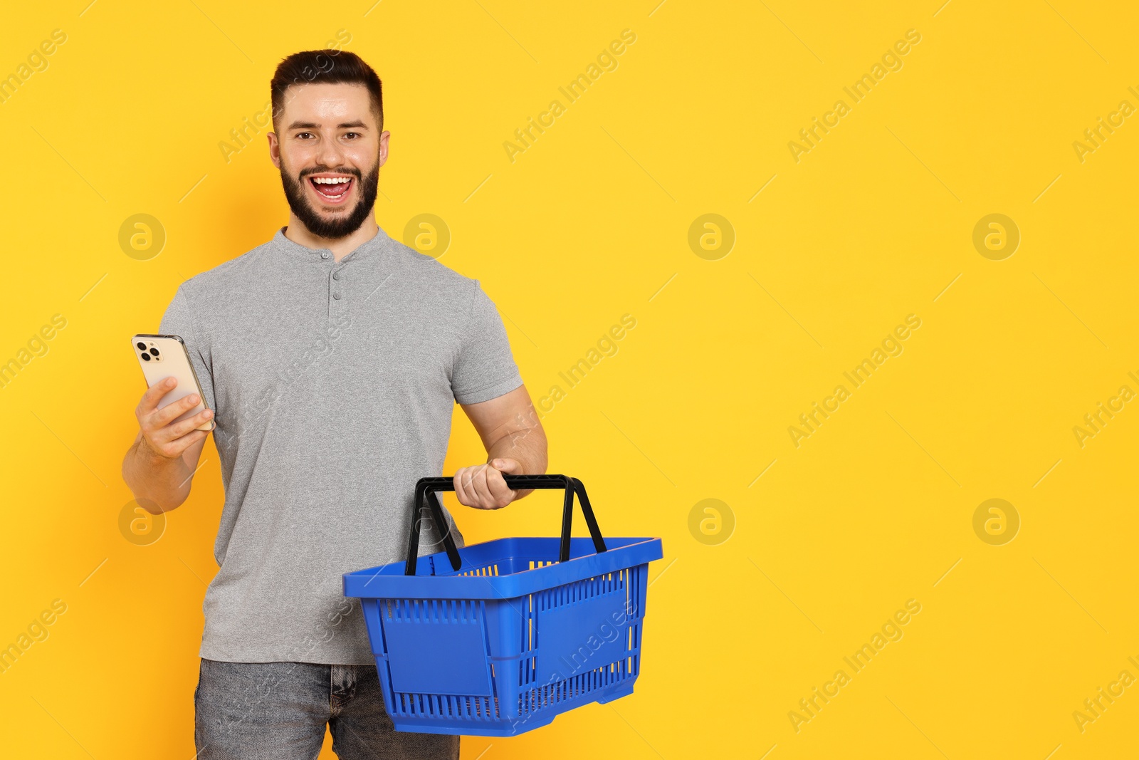 Man with empty shopping basket and smartphone on orange background, space for text Photo of Man with empty shopping basket and smartphone on orange background, space for text