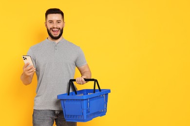 Photo of Man with empty shopping basket and smartphone on orange background, space for text