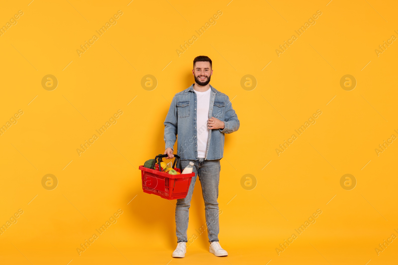 Man with shopping basket full of products on orange background Photo of Man with shopping basket full of products on orange background
