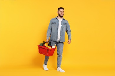 Photo of Man with shopping basket full of products on orange background