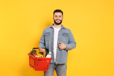 Photo of Man with shopping basket full of products on orange background