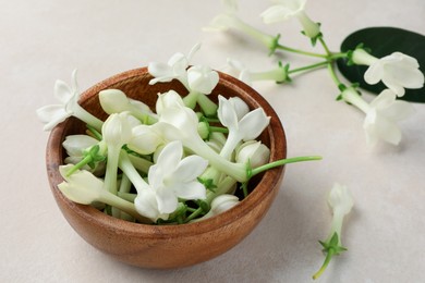 Photo of Bowl with jasmine flowers on beige table, closeup