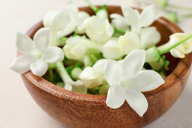 Photo of Bowl with jasmine flowers on beige table, closeup