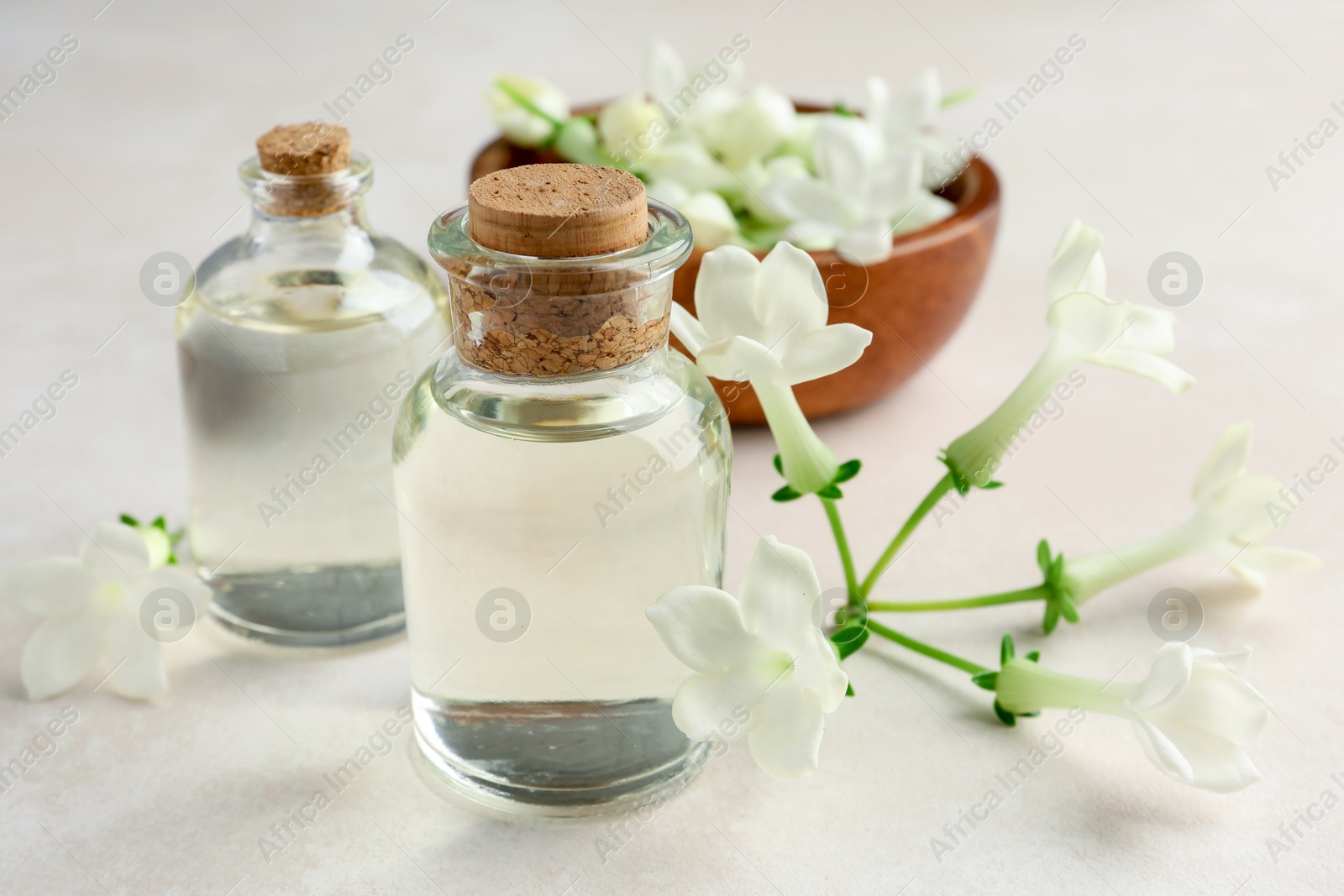 Photo of Bottles of essential oils and jasmine flowers on beige table, closeup