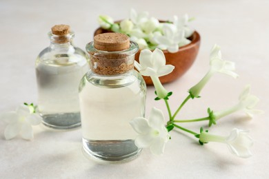 Photo of Bottles of essential oils and jasmine flowers on beige table, closeup