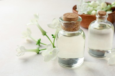Photo of Bottles of essential oils and jasmine flowers on beige table, closeup