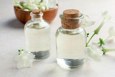 Photo of Bottles of essential oils and jasmine flowers on beige table, closeup