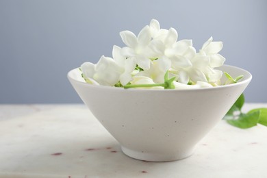 Photo of Beautiful jasmine flowers in bowl on table, closeup. Space for text