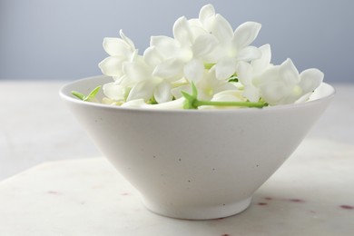 Photo of Beautiful jasmine flowers in bowl on table, closeup