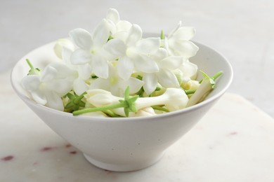 Photo of Beautiful jasmine flowers in bowl on table, closeup