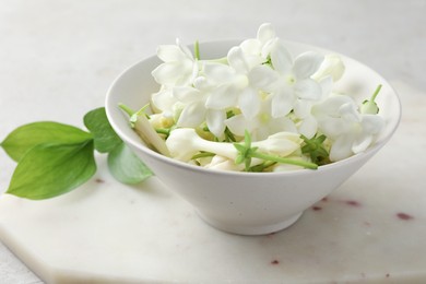 Photo of Beautiful jasmine flowers in bowl and green leaves on table, closeup