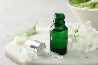 Photo of Bottle of essential oil and jasmine flowers on table, closeup
