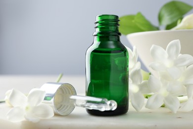 Photo of Bottle of essential oil and jasmine flowers on table, closeup