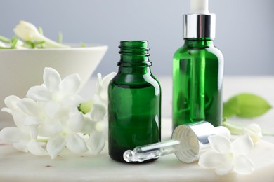 Photo of Bottles of essential oils and jasmine flowers on table, closeup