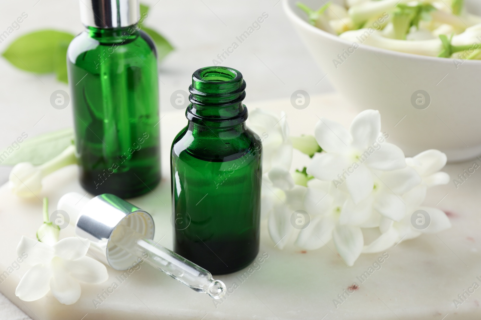 Bottles of essential oils and jasmine flowers on table, closeup Photo of Bottles of essential oils and jasmine flowers on table, closeup