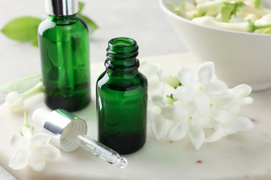 Photo of Bottles of essential oils and jasmine flowers on table, closeup