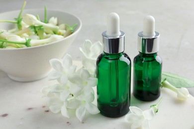 Photo of Bottles of essential oils and jasmine flowers on table, closeup