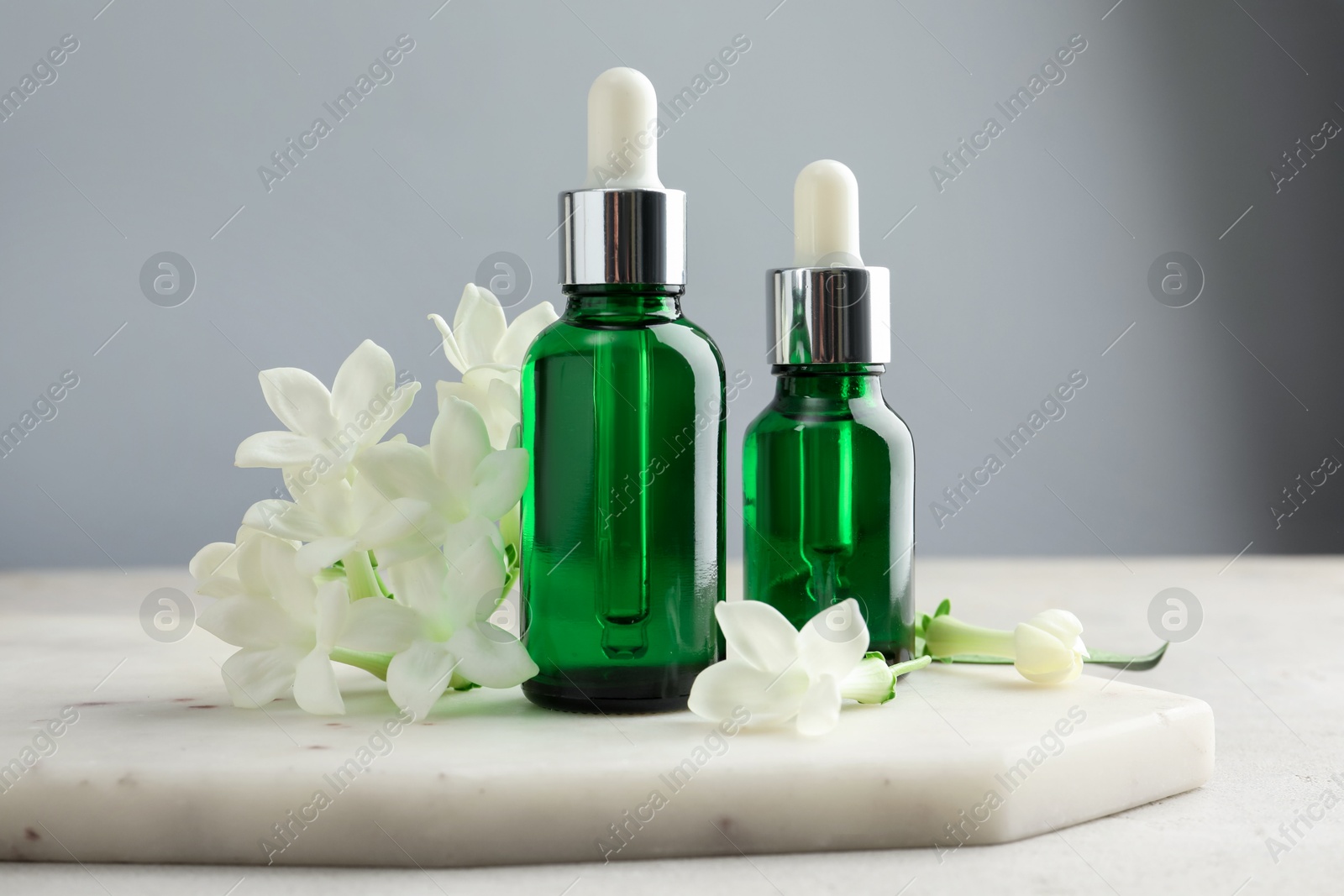 Photo of Bottles of essential oils and jasmine flowers on light grey table, closeup
