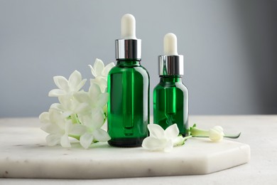 Photo of Bottles of essential oils and jasmine flowers on light grey table, closeup