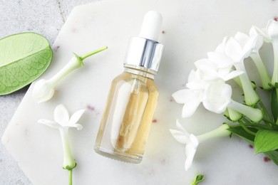 Photo of Bottle of essential oil and jasmine flowers on light grey table, top view