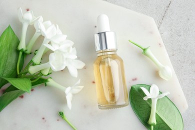 Photo of Bottle of essential oil and jasmine flowers on light grey table, top view