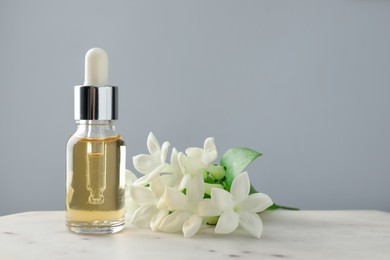 Photo of Bottle of essential oil and jasmine flowers on table against grey background