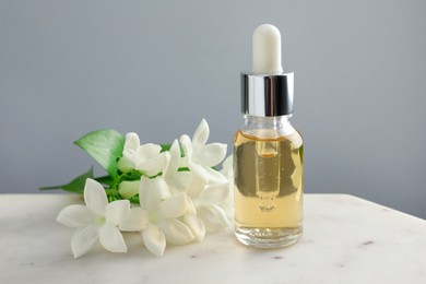 Photo of Bottle of essential oil and jasmine flowers on table against grey background, closeup