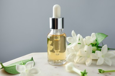 Photo of Bottle of essential oil and jasmine flowers on table against grey background, closeup