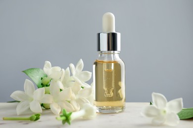 Photo of Bottle of essential oil and jasmine flowers on table against grey background, closeup