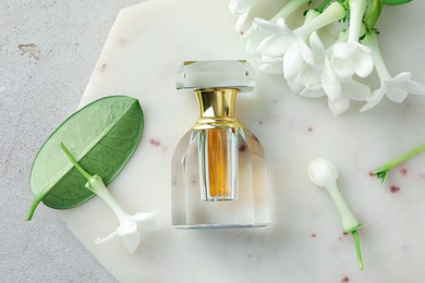 Photo of Perfume and jasmine flowers on light grey table, top view