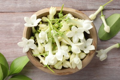 Photo of Beautiful jasmine flowers in bowl and green leaves on wooden table, flat lay