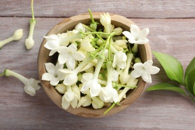 Photo of Beautiful jasmine flowers in bowl and green leaves on wooden table, flat lay