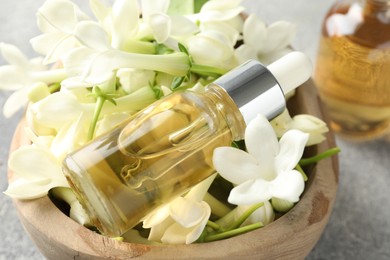 Photo of Bottle of essential oil and jasmine flowers in bowl on table, closeup
