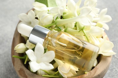 Photo of Bottle of essential oil and jasmine flowers in bowl on table, closeup