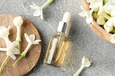 Photo of Bottle of essential oil and jasmine flowers on grey table, flat lay